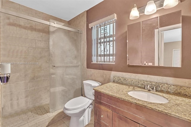 bathroom with a shower with door, toilet, tile patterned flooring, vanity, and tile walls