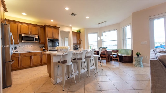 kitchen featuring backsplash, decorative light fixtures, appliances with stainless steel finishes, an island with sink, and a kitchen bar