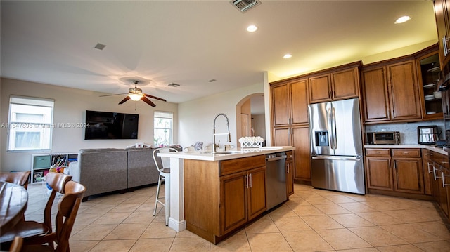 kitchen featuring appliances with stainless steel finishes, an island with sink, a kitchen bar, sink, and ceiling fan