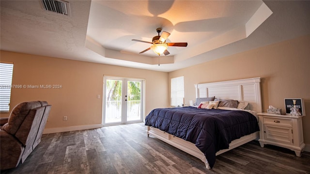 bedroom with dark wood-type flooring, a tray ceiling, access to exterior, and ceiling fan