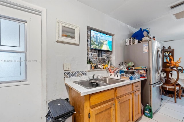 kitchen with light tile patterned floors, sink, kitchen peninsula, and stainless steel fridge