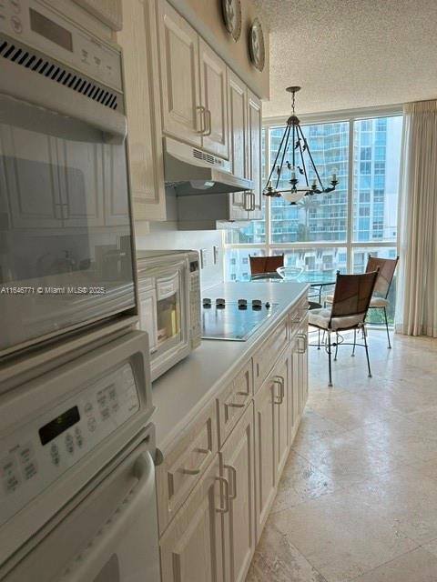 kitchen featuring pendant lighting, white appliances, an inviting chandelier, expansive windows, and a textured ceiling