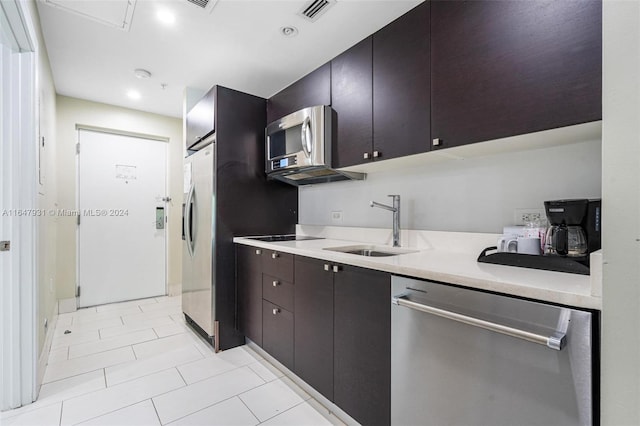 kitchen featuring stainless steel appliances, dark brown cabinetry, sink, a barn door, and light tile patterned flooring