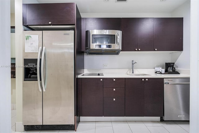 kitchen with sink, stainless steel appliances, light tile patterned flooring, and dark brown cabinetry