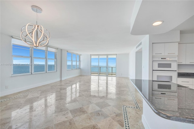 tiled spare room featuring a chandelier, a wall of windows, and a water view