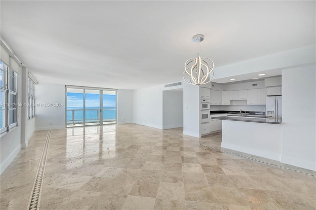 unfurnished living room with an inviting chandelier, sink, a water view, light tile patterned floors, and floor to ceiling windows