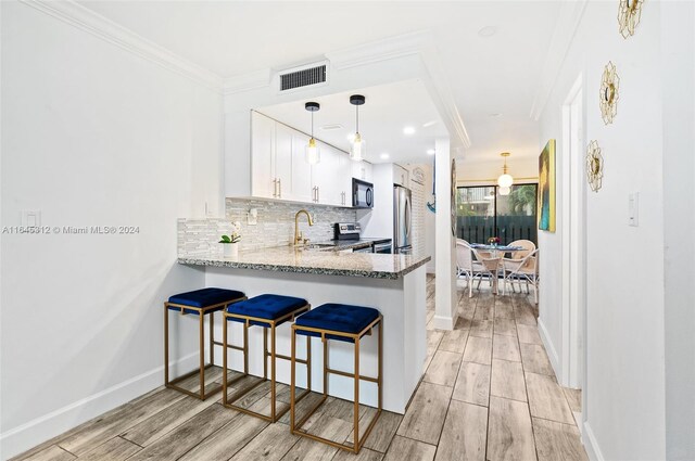 kitchen with decorative light fixtures, stainless steel appliances, light wood-type flooring, light stone countertops, and white cabinets