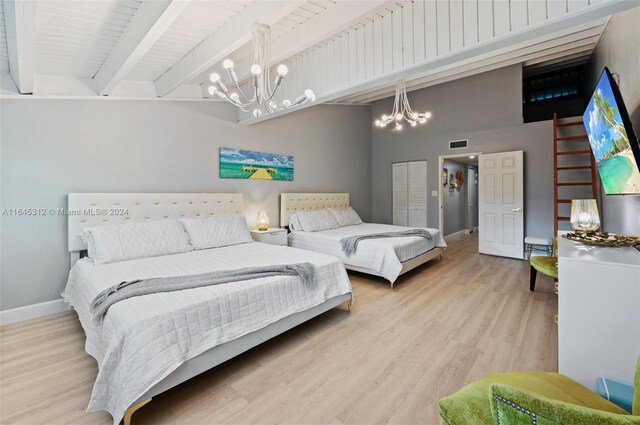 bedroom with light hardwood / wood-style floors, beam ceiling, an inviting chandelier, and a closet