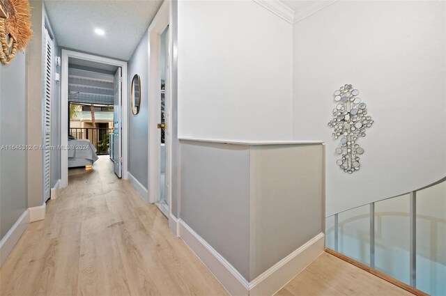 hallway featuring a notable chandelier, a textured ceiling, light hardwood / wood-style flooring, and crown molding