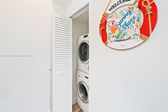 clothes washing area with wood-type flooring and stacked washer / dryer