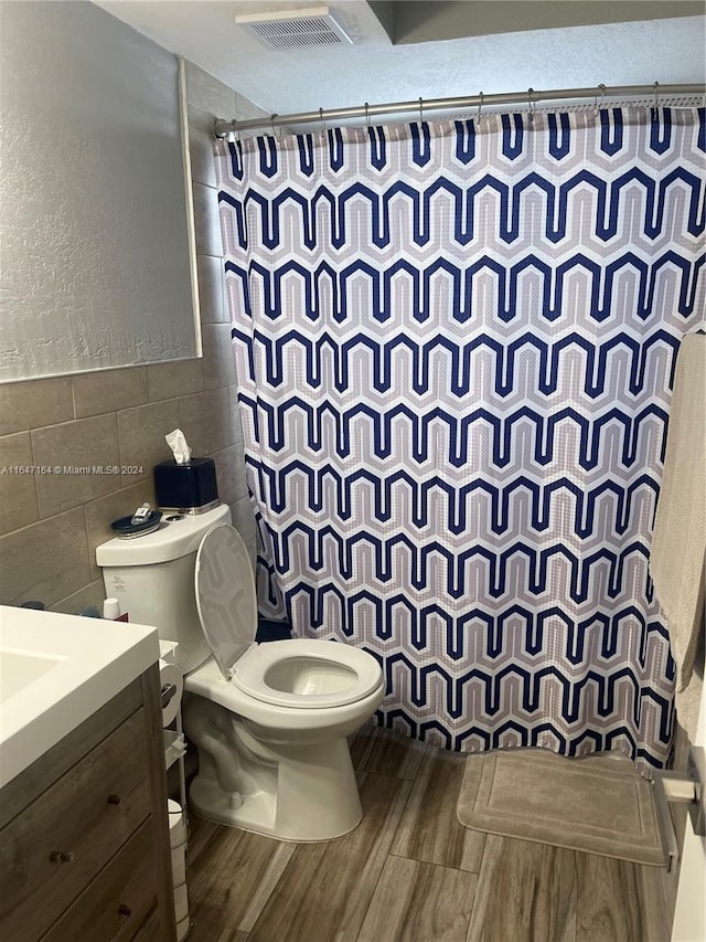 bathroom with walk in shower, vanity, wood-type flooring, tile walls, and toilet