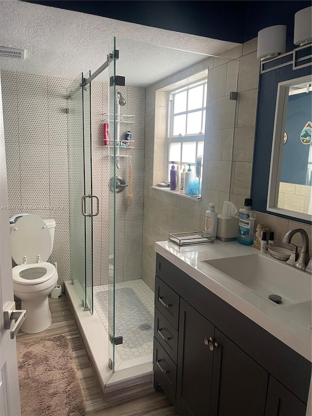 bathroom featuring wood-type flooring, an enclosed shower, a textured ceiling, toilet, and vanity