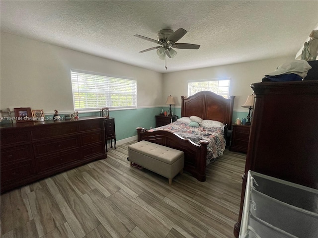 bedroom featuring a textured ceiling, light hardwood / wood-style floors, multiple windows, and ceiling fan