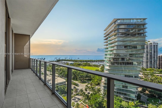 balcony at dusk featuring a water view and a city view