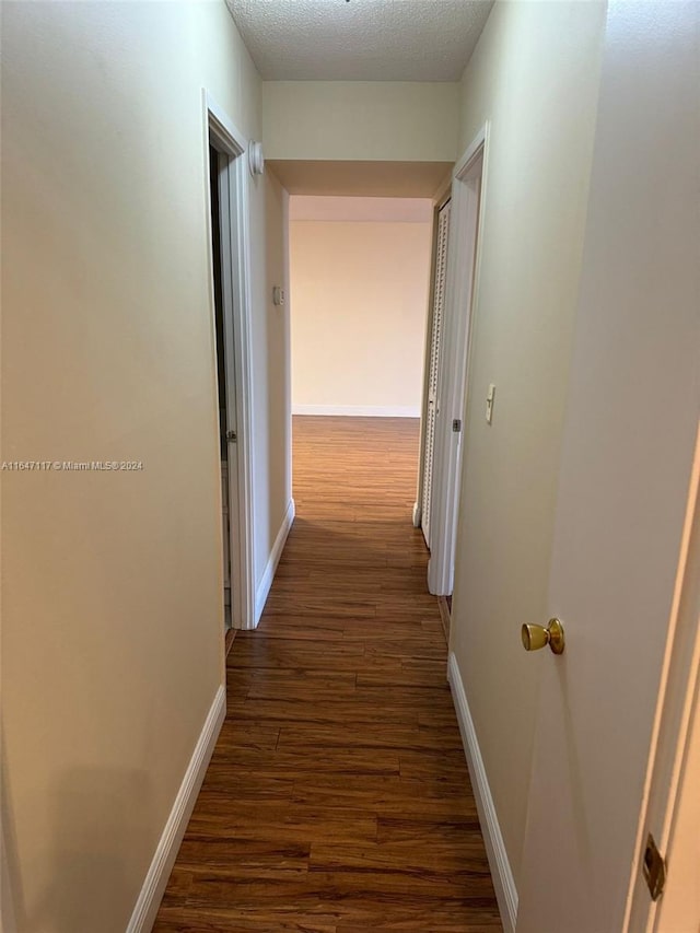 hall with a textured ceiling and dark hardwood / wood-style flooring