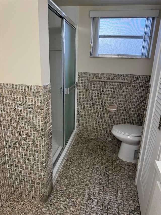 bathroom with tile walls, toilet, and a shower with shower door