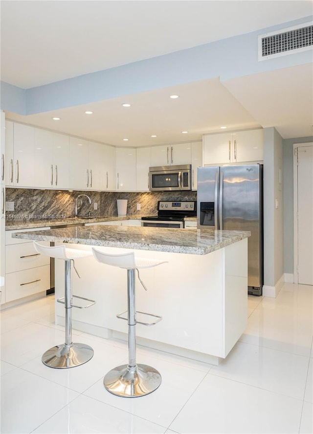 kitchen with white cabinetry, backsplash, stainless steel appliances, and a breakfast bar area