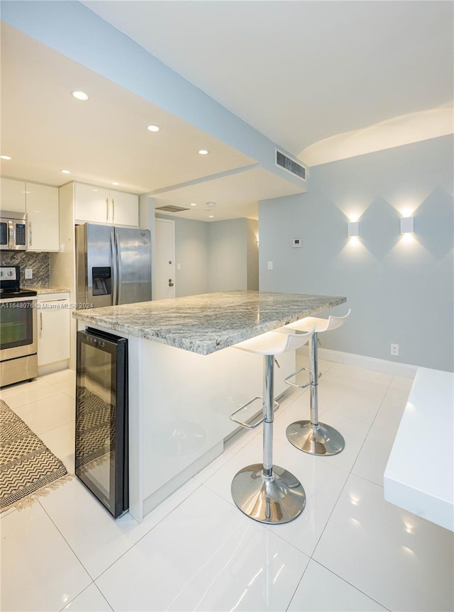 kitchen with stainless steel appliances, a breakfast bar, beverage cooler, white cabinetry, and tasteful backsplash