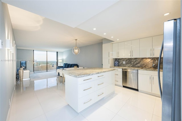 kitchen with decorative backsplash, white cabinets, a kitchen island, decorative light fixtures, and stainless steel appliances