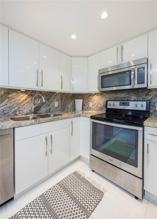 kitchen with tasteful backsplash, light tile patterned floors, appliances with stainless steel finishes, white cabinetry, and sink