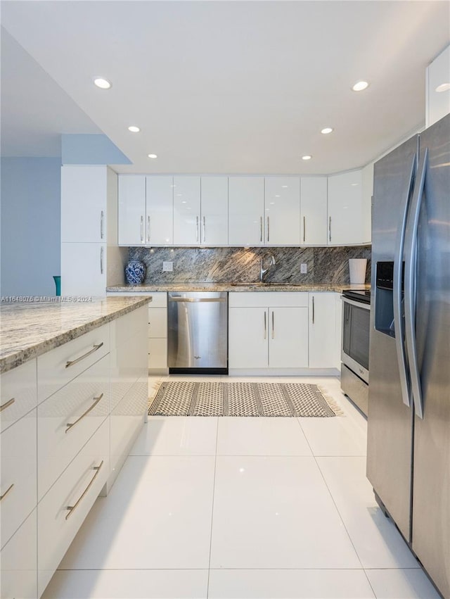 kitchen with light stone counters, light tile patterned floors, backsplash, white cabinetry, and stainless steel appliances