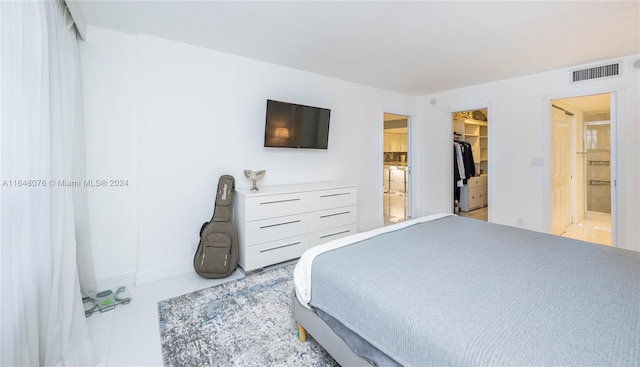 tiled bedroom featuring a closet, ensuite bath, and a walk in closet