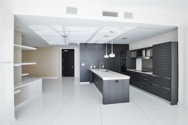 kitchen featuring light tile patterned floors, an island with sink, black electric cooktop, sink, and decorative light fixtures