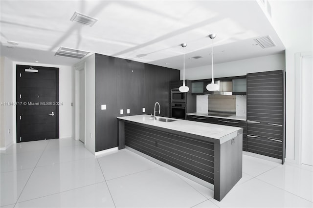 kitchen with black electric stovetop, sink, pendant lighting, light tile patterned floors, and a kitchen island with sink