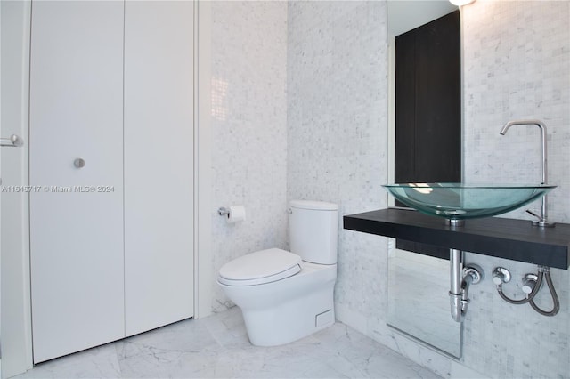 bathroom with toilet, sink, and tile walls