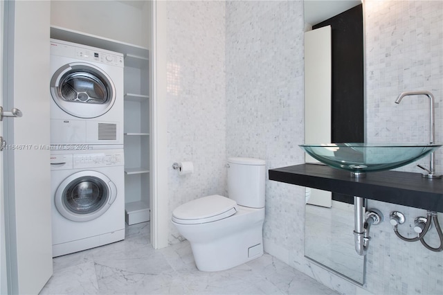 bathroom with toilet, sink, and stacked washer and clothes dryer