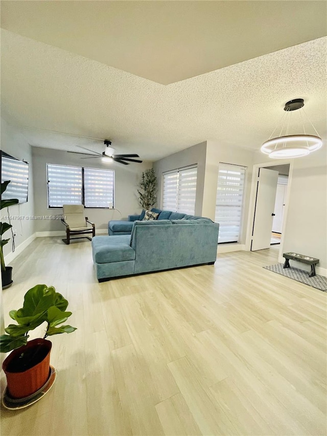 living room with ceiling fan, light wood-type flooring, and a textured ceiling