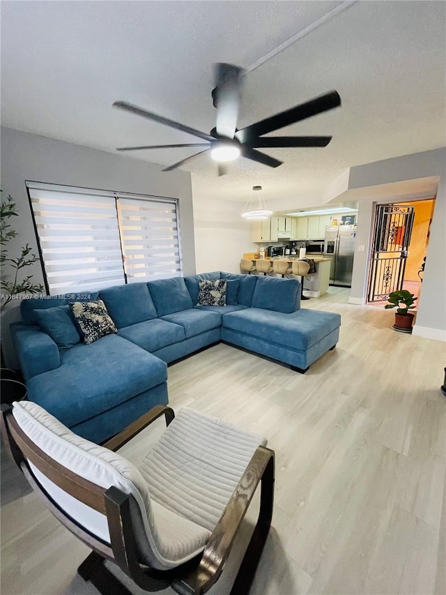 living room featuring ceiling fan, light wood-type flooring, and a textured ceiling