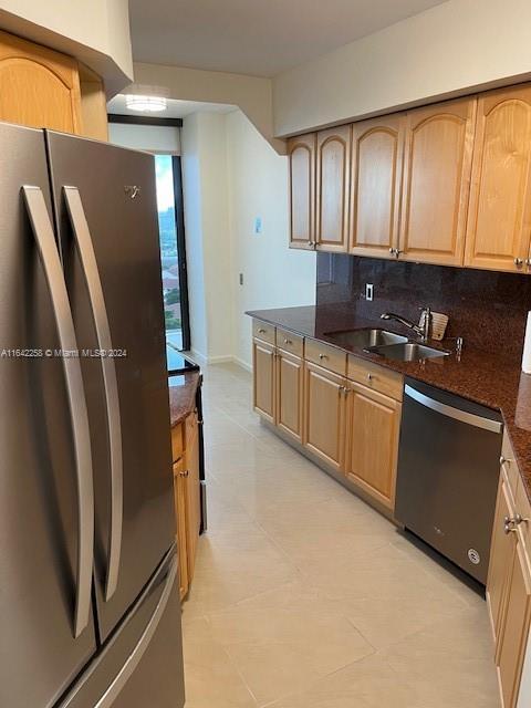 kitchen with stainless steel appliances, a sink, baseboards, backsplash, and dark stone counters