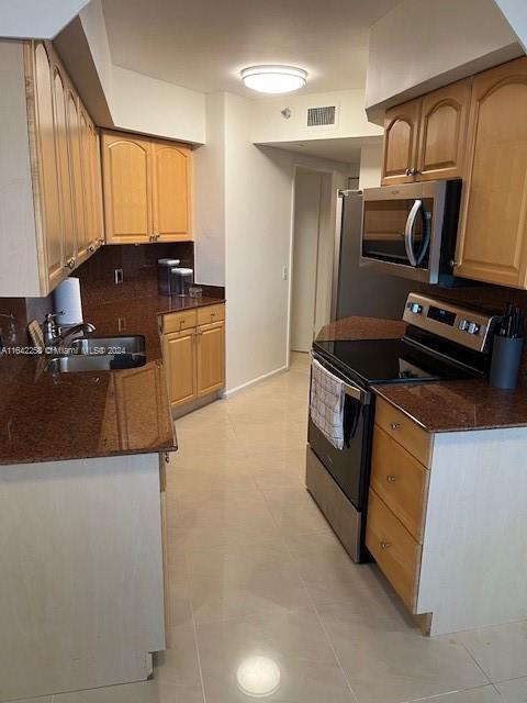 kitchen with dark stone countertops, light tile patterned floors, appliances with stainless steel finishes, sink, and tasteful backsplash