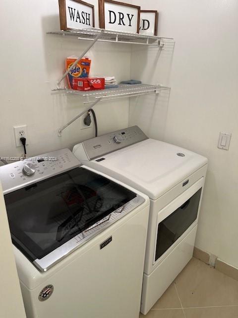 washroom with laundry area, baseboards, light tile patterned flooring, and washing machine and clothes dryer