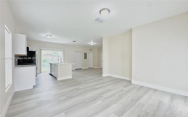 kitchen with light hardwood / wood-style floors, white cabinets, a kitchen island with sink, and sink