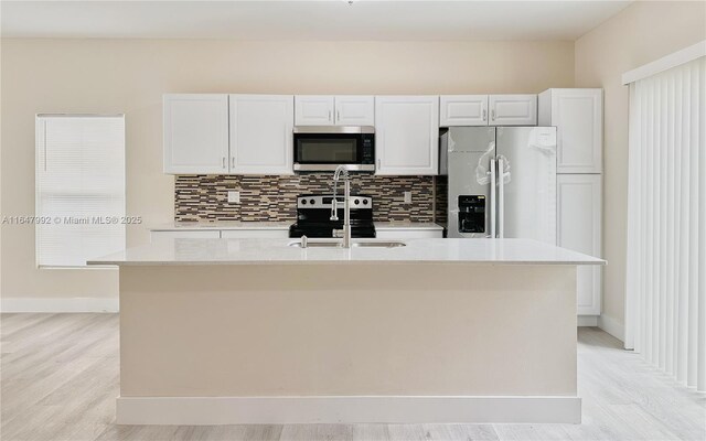 kitchen with light hardwood / wood-style flooring, stainless steel appliances, white cabinetry, and an island with sink