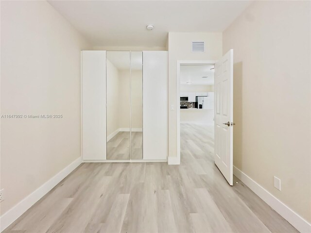 unfurnished bedroom with a closet, light wood-type flooring, and white fridge with ice dispenser