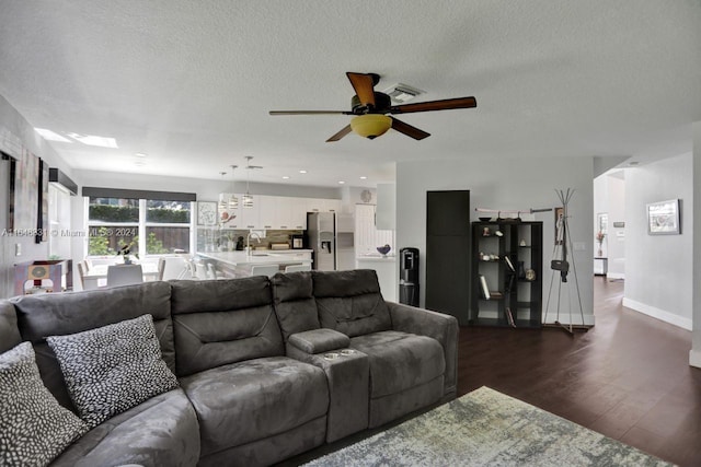 living room with ceiling fan, dark hardwood / wood-style flooring, and a textured ceiling