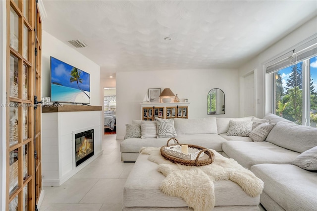 living area with a glass covered fireplace, light tile patterned flooring, and visible vents