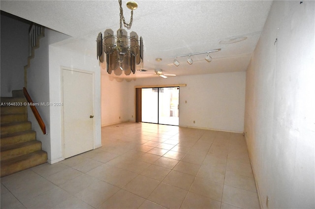 empty room with light tile patterned floors, stairway, rail lighting, a textured ceiling, and ceiling fan with notable chandelier