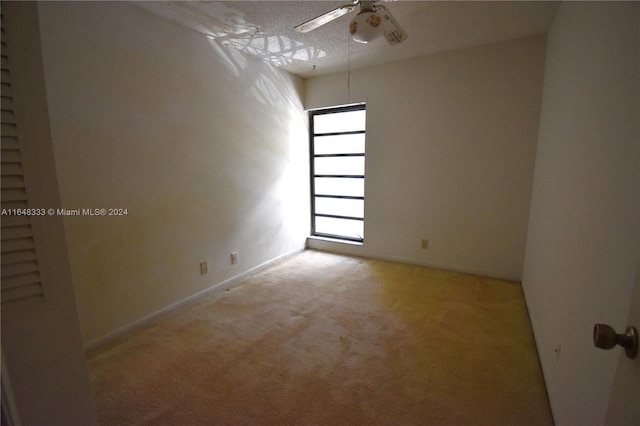 spare room featuring light carpet, a ceiling fan, and baseboards