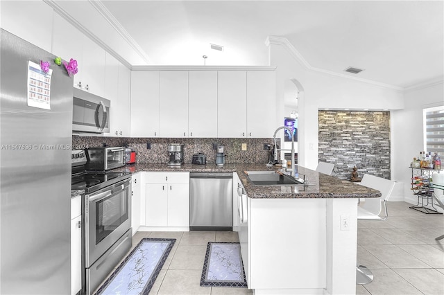 kitchen featuring lofted ceiling, stainless steel appliances, kitchen peninsula, and white cabinets