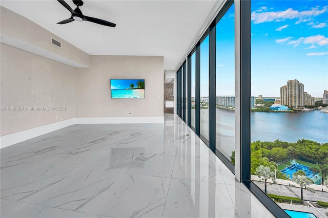 unfurnished room with a wall of windows, a water view, and ceiling fan