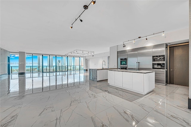 kitchen featuring a center island, white cabinets, track lighting, sink, and floor to ceiling windows