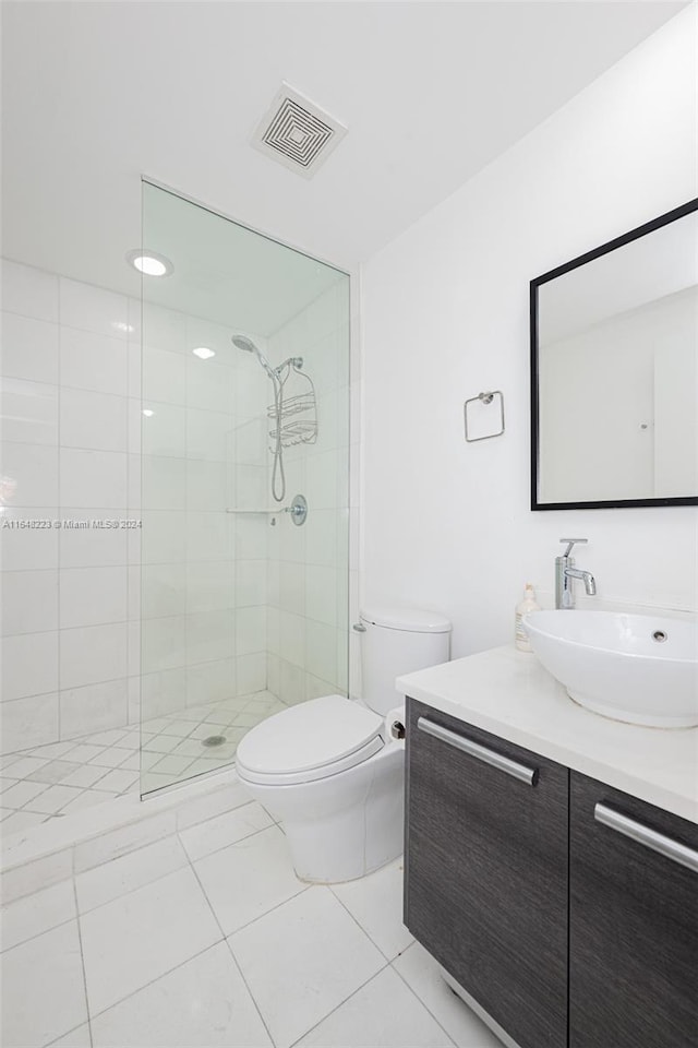 bathroom featuring tile patterned flooring, toilet, a tile shower, and vanity