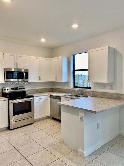 kitchen featuring light tile patterned flooring, sink, stainless steel appliances, and kitchen peninsula