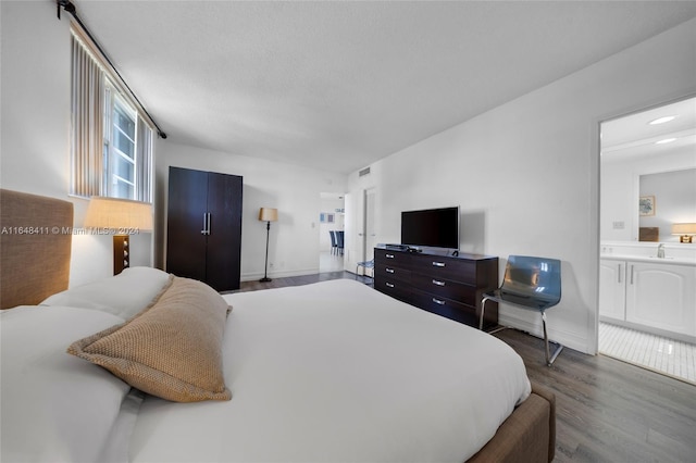 bedroom featuring hardwood / wood-style floors, ensuite bathroom, sink, and a textured ceiling