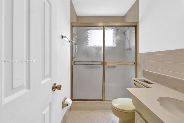 bathroom with vanity, tile patterned floors, toilet, tile walls, and a shower with shower door