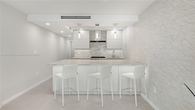 kitchen with decorative backsplash, sink, wall chimney range hood, white cabinets, and a breakfast bar area